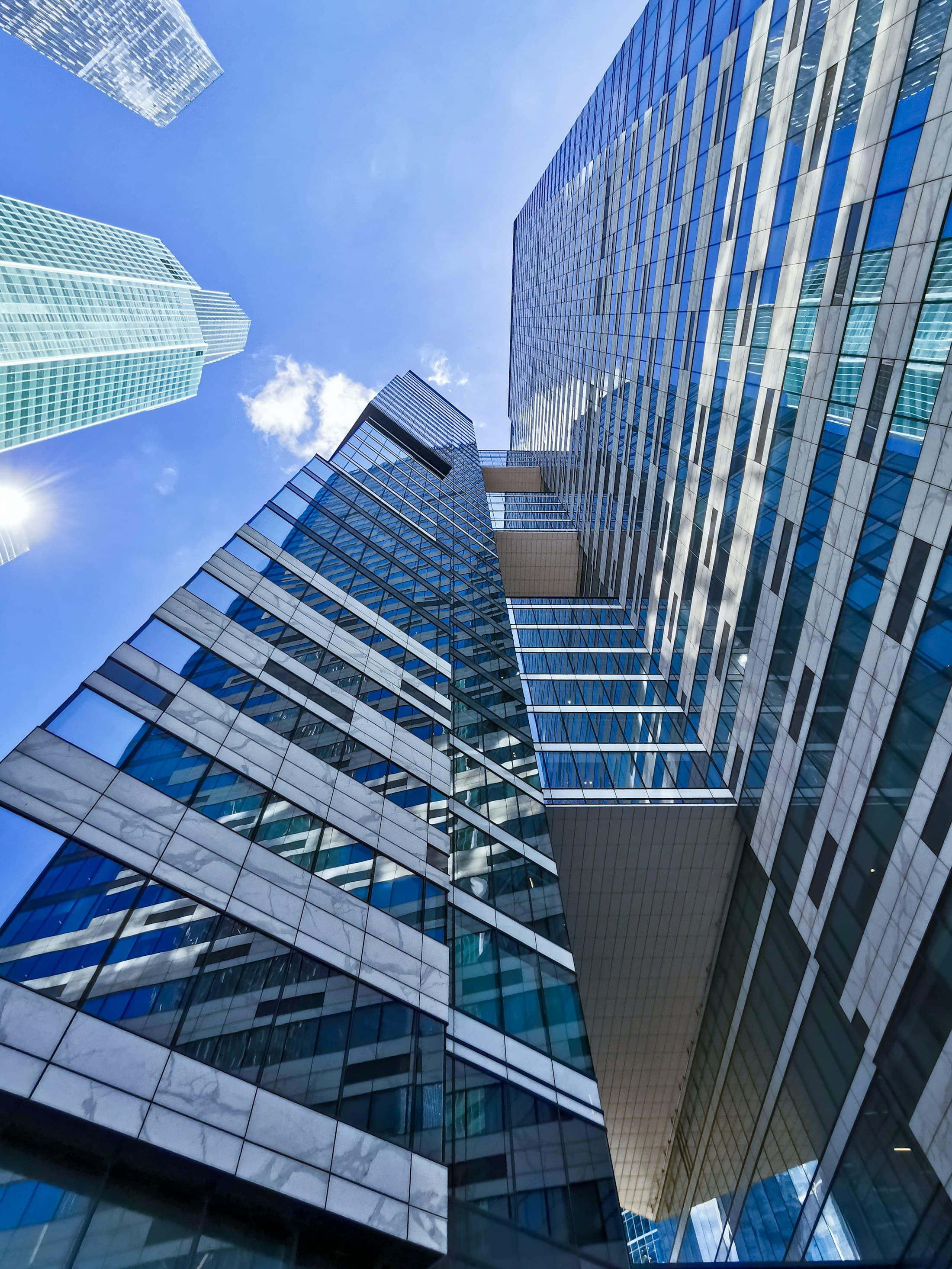 An upward perspective through sculptural glass towers into the open sky